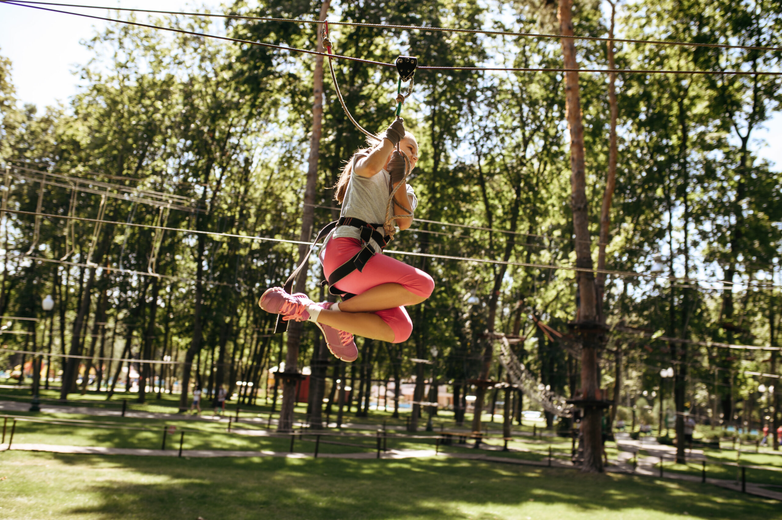 Little brave girl on zipline in rope park, playground. Child climbing on suspension bridge, extreme sport adventure on vacations, danger entertainment outdoors